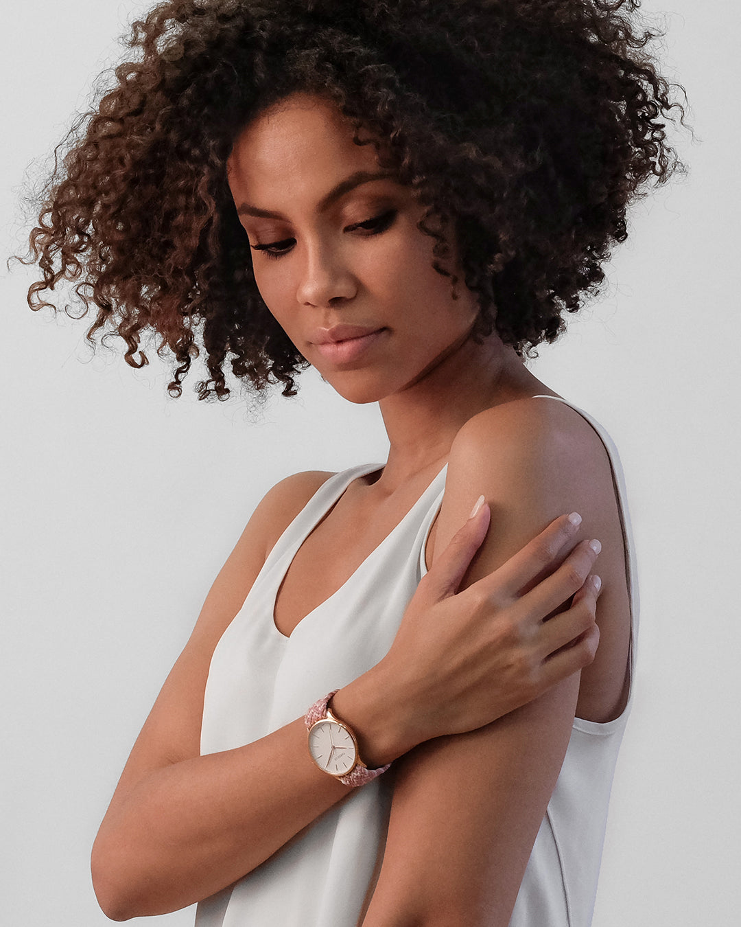 Jeune femme souriante portant une montre Tweed Co. avec bracelet tressé rose sur fond urbain